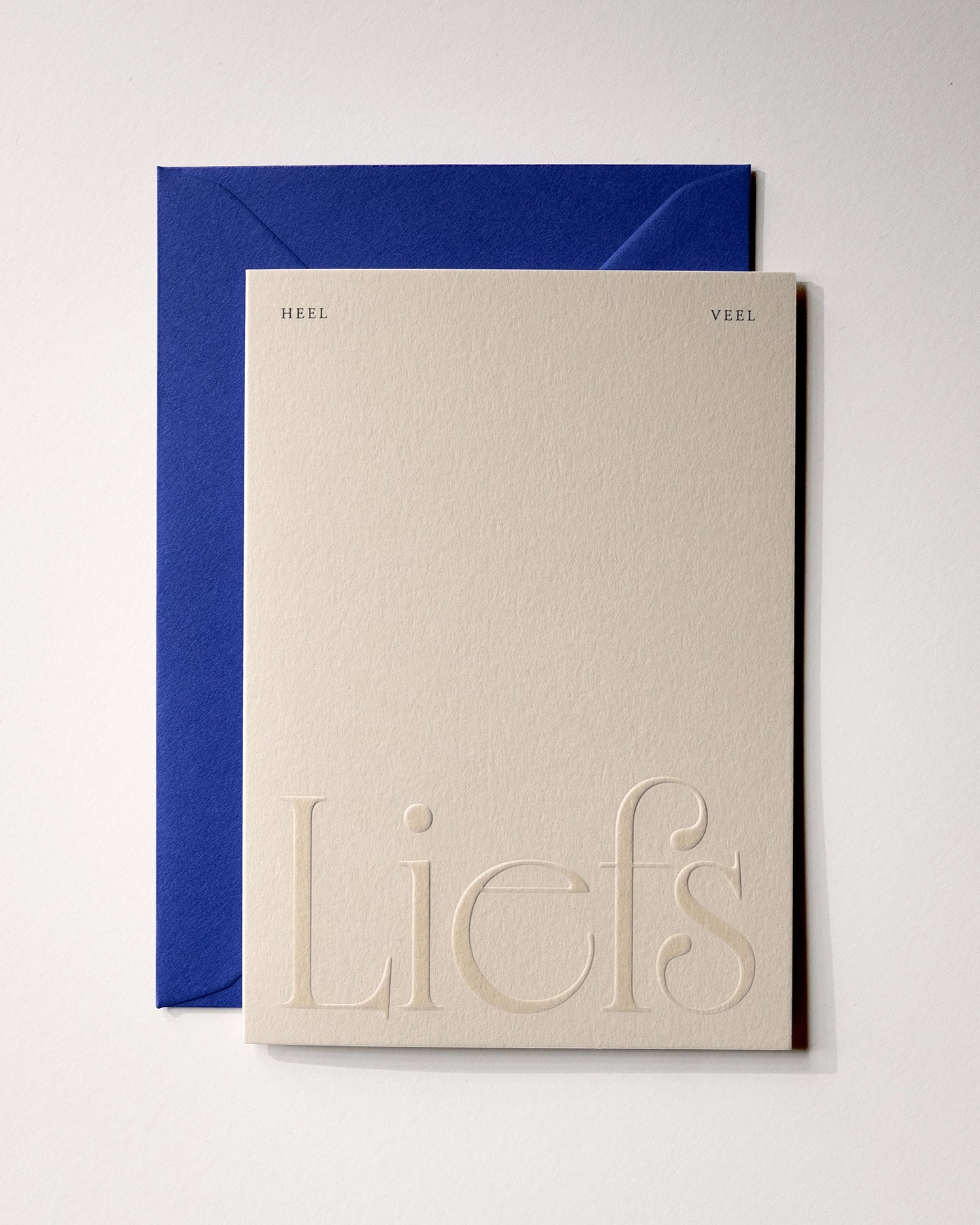 Top view of minimal luxury embossed friendship card “heel veel liefs” on Colorplan Mist paper with royal blue envelope