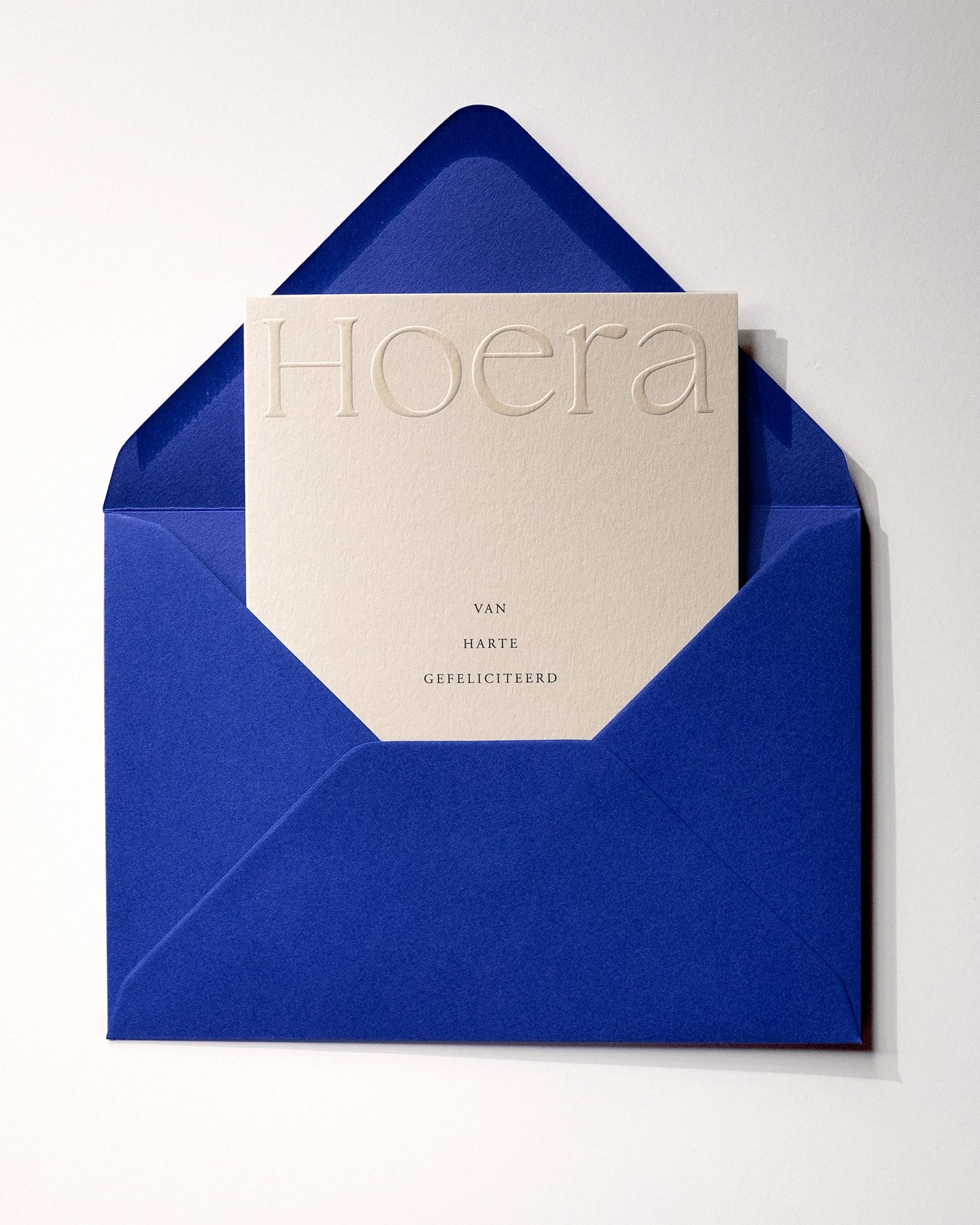 Flat lay of minimal luxury embossed birthday card “hoera van harte gefeliciteerd” inside royal blue envelop on Colorplan Mist paper