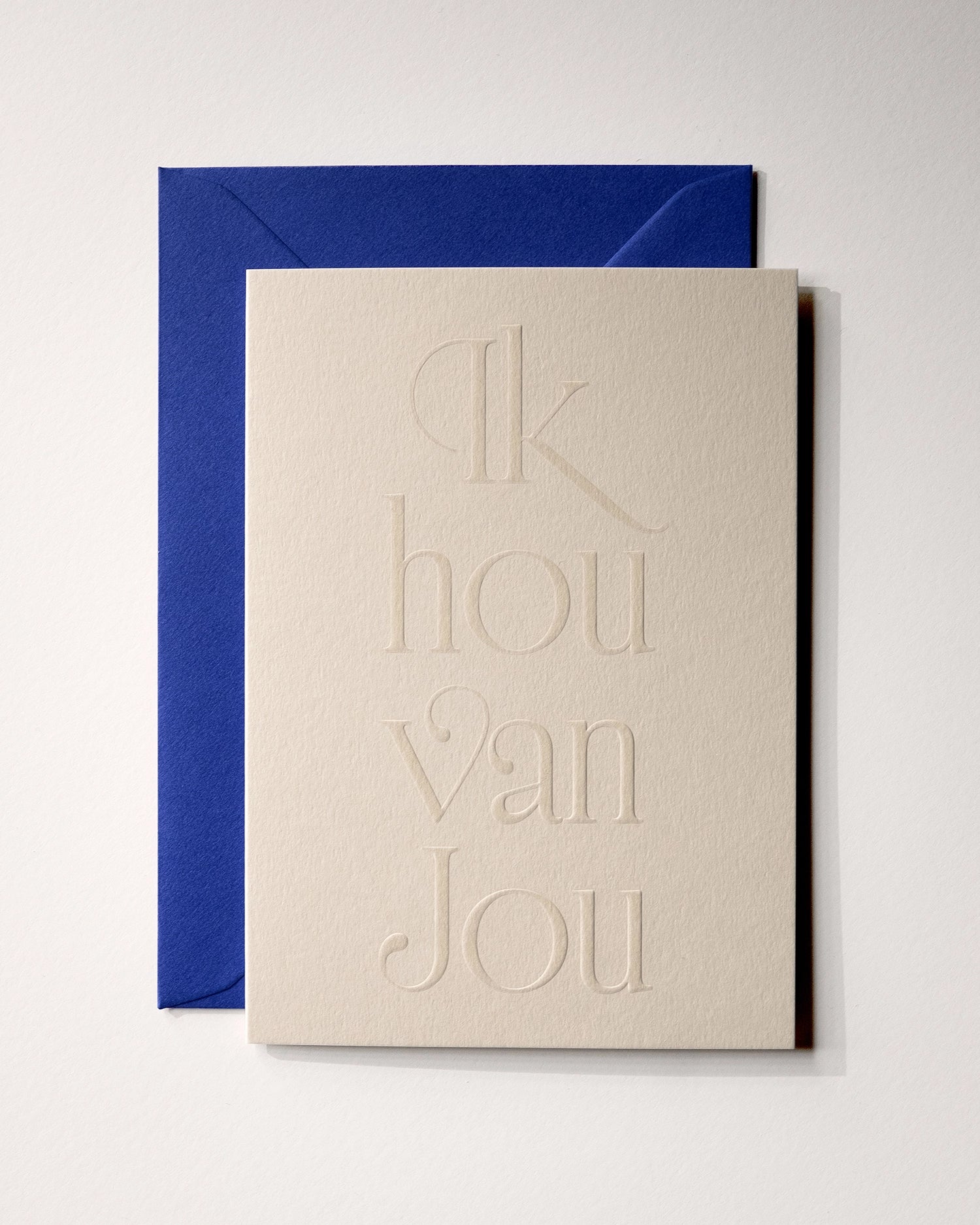 Top view of minimal luxury embossed love card “ik hou van jou” on Colorplan Mist paper with royal blue envelope