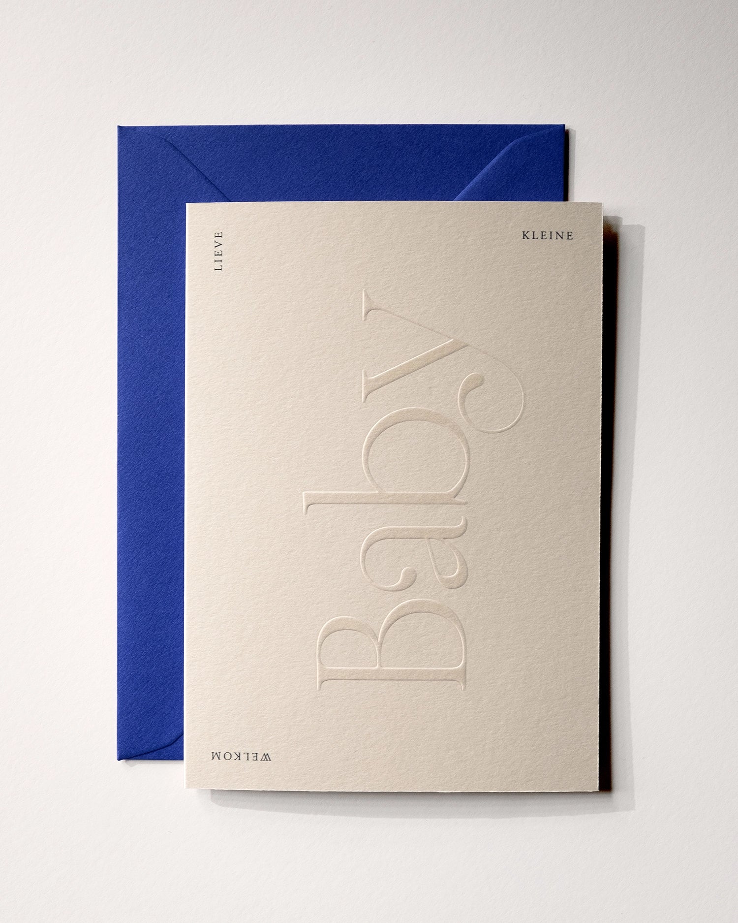 Top view of minimal luxury embossed new baby card “welkom lieve kleine baby” on Colorplan Mist paper with royal blue envelope