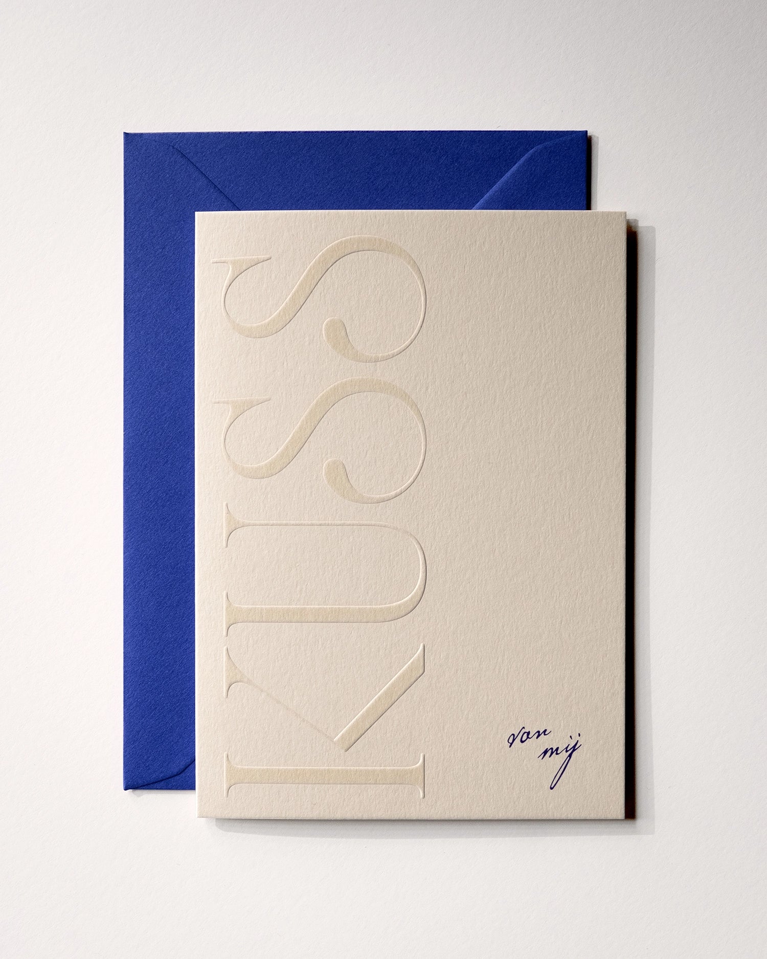 Top view of minimal luxury embossed greeting card “kuss van mij” on Colorplan Mist paper with royal blue envelope