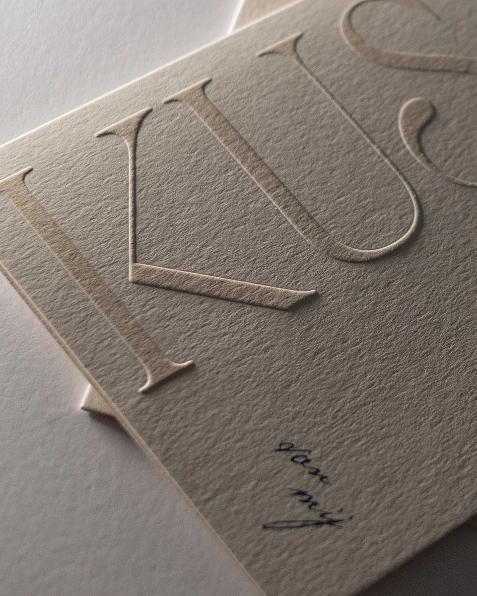 Stacked minimal luxury greeting cards "Kuss van mij" showing embossed detail with shadows on Colorplan Mist paper