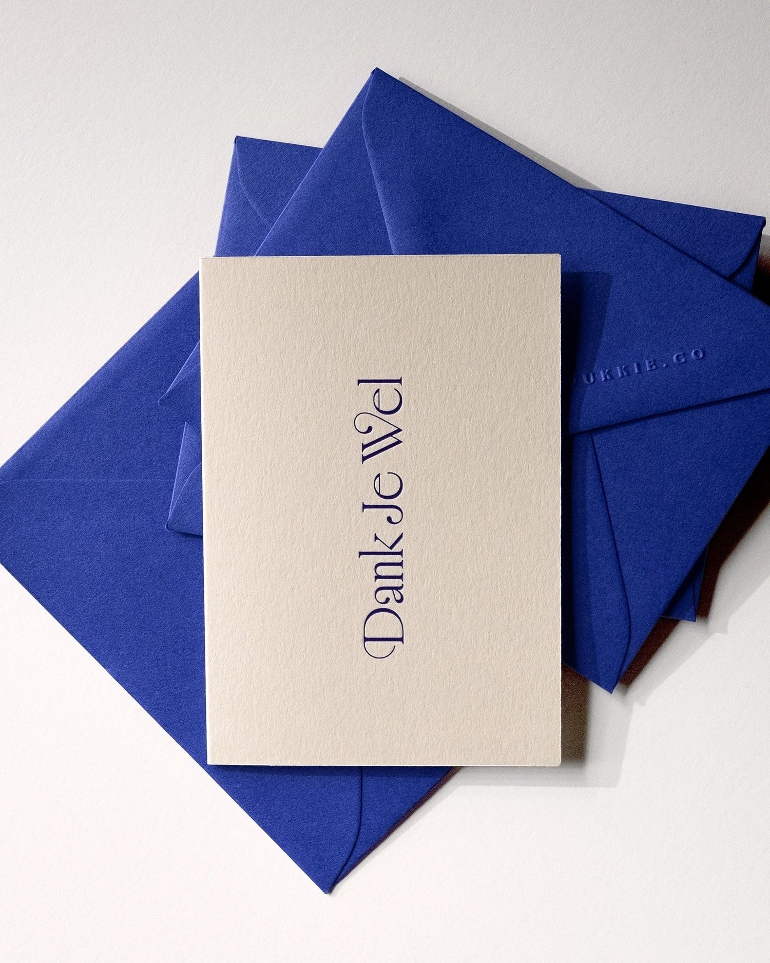 Flat lay of minimal luxury letterpress thank you card “dank je wel” on stack of playful royal blue envelopes