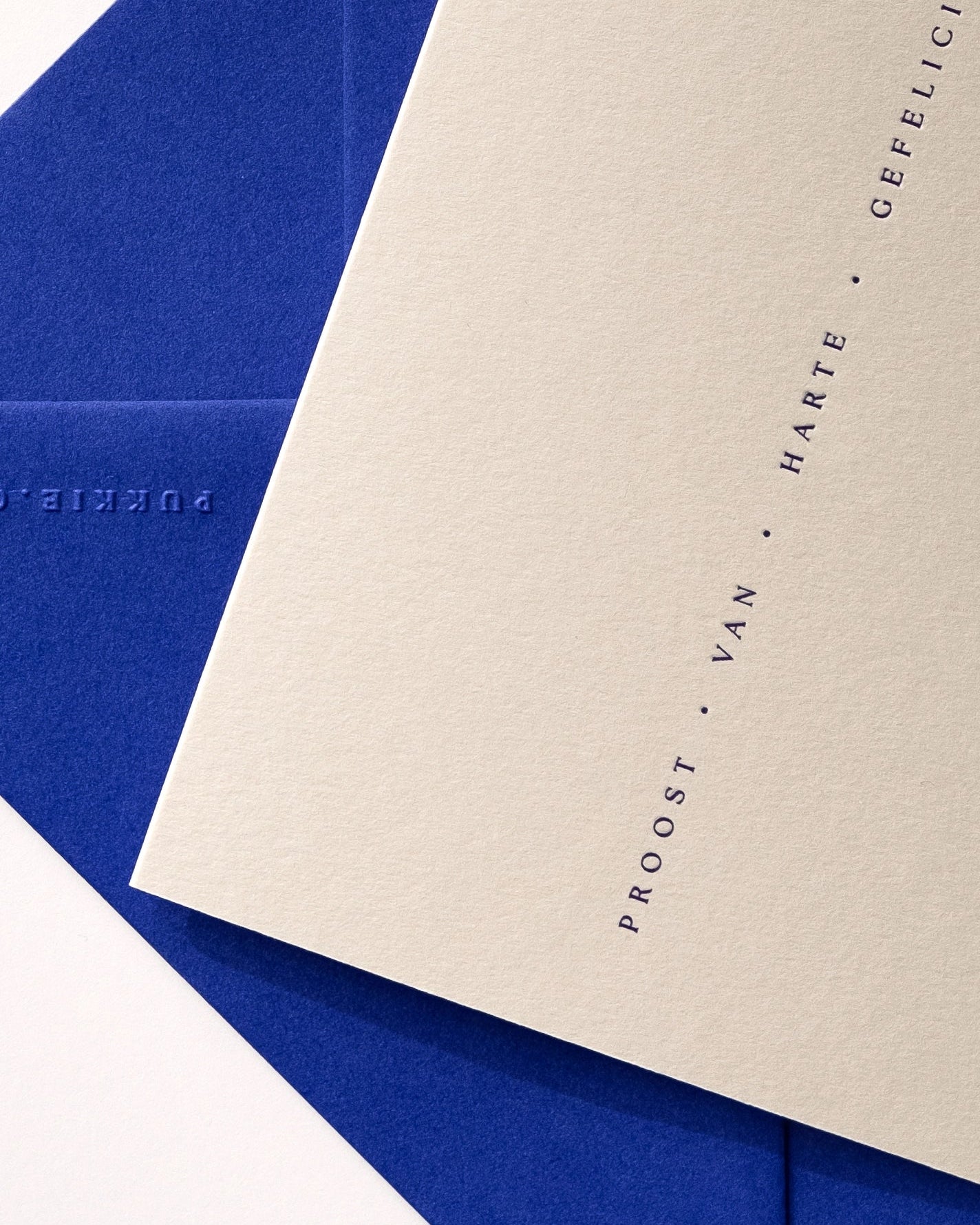 Close-up of minimal luxury letterpress celebration card “proost van harte gefeliciteerd” with royal blue envelope on Colorplan Mist paper