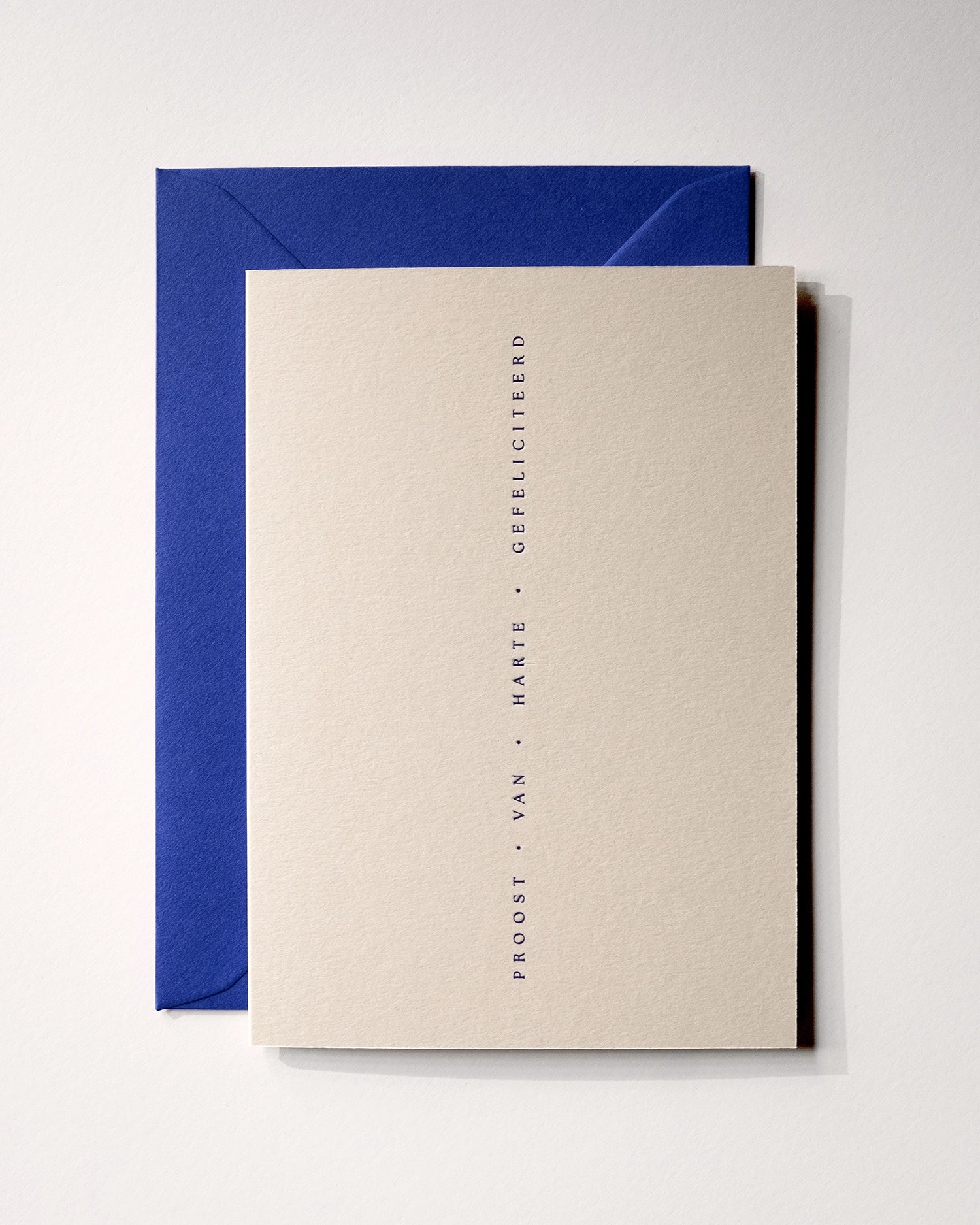 Top view of minimal luxury letterpress celebration card “proost van harte gefeliciteerd” on Colorplan Mist paper with royal blue envelope