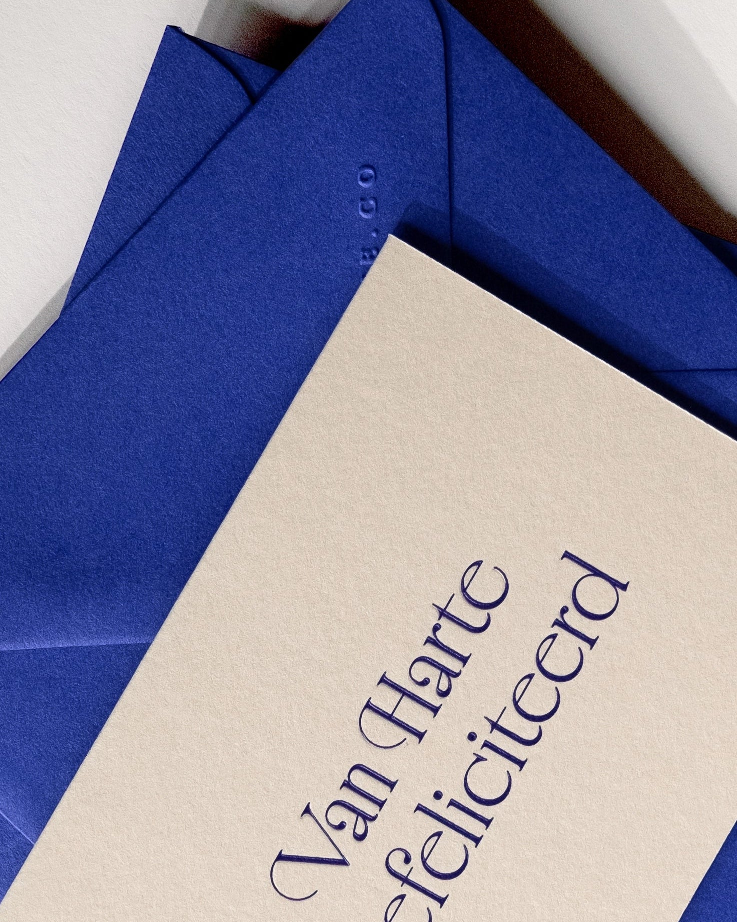 Close-up of minimal luxury letterpress brithday card “van harte gefeliciteerd” with royal blue envelope on Colorplan Mist paper