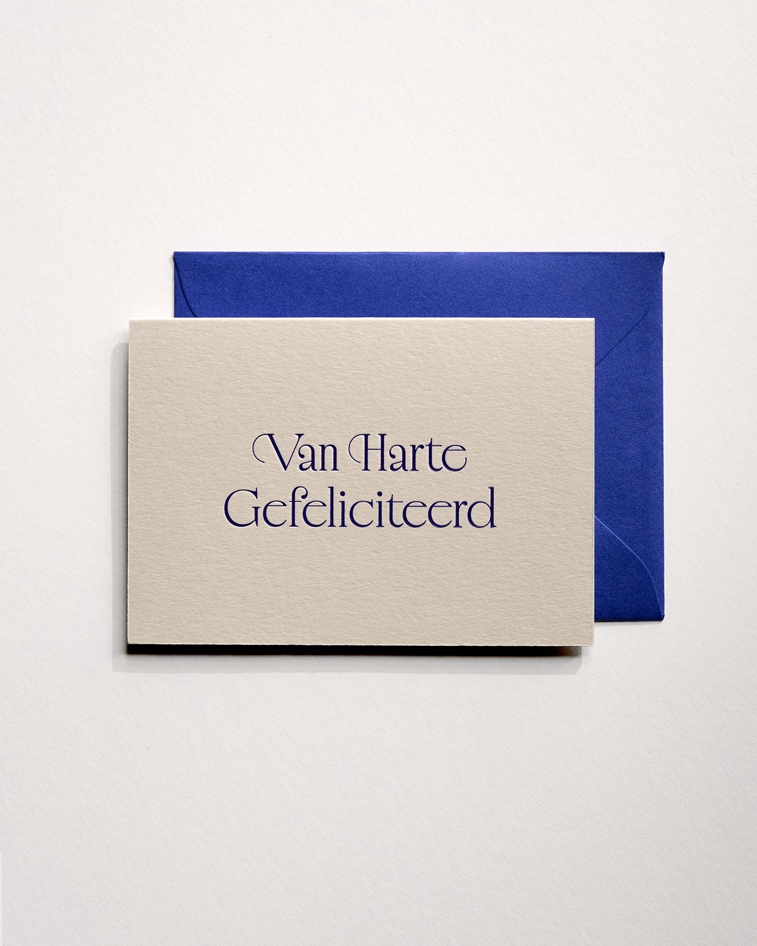 Top view of minimal luxury letterpress brithday card “van harte gefeliciteerd” on Colorplan Mist paper with royal blue envelope