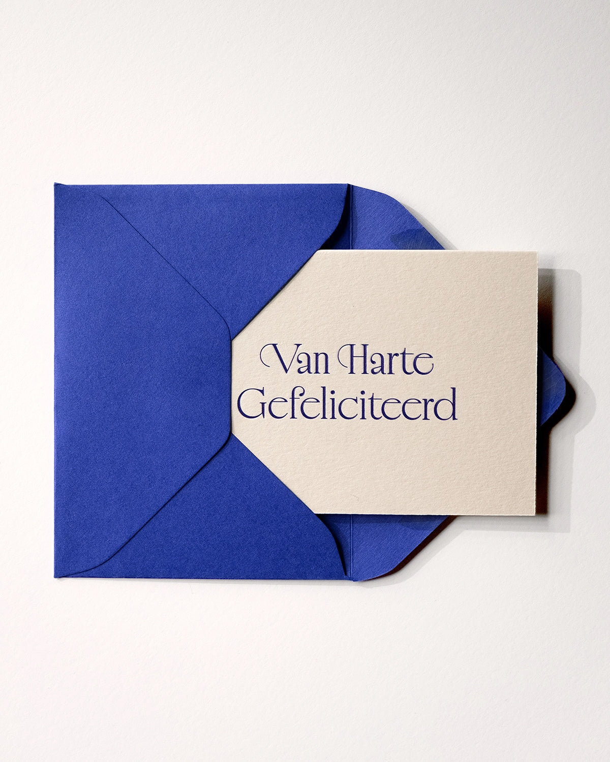 Flat lay of minimal luxury letterpress brithday card “van harte gefeliciteerd” inside royal blue envelop on Colorplan Mist paper